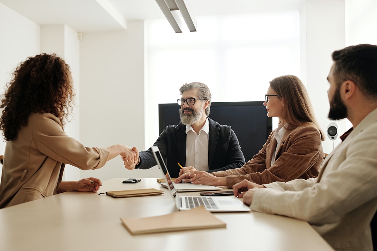 Man shaking hands with a woman while two other people watch a conference table